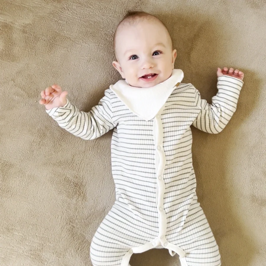 En glad baby som ligger paa ryggen paa Babynordic taeppet