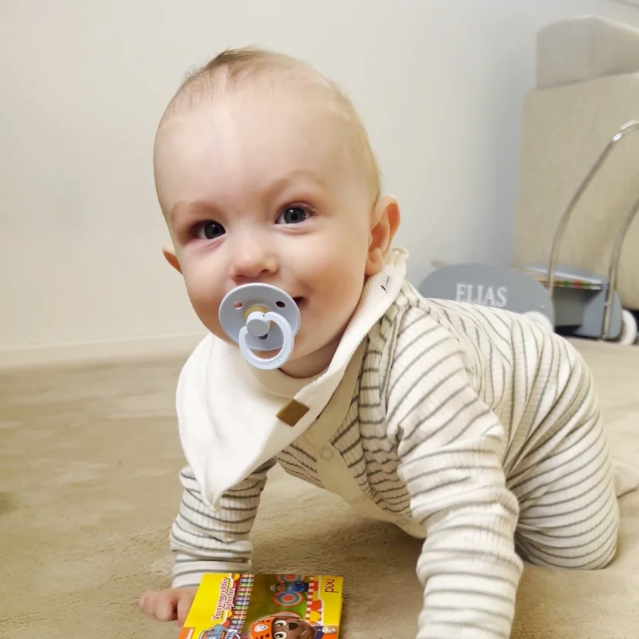 En smilende og glad baby paa et lille beige BabyNordic taeppe